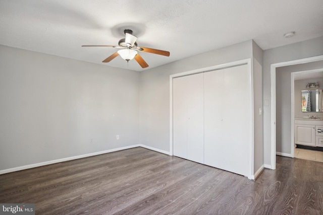 unfurnished bedroom with dark wood-type flooring, sink, ensuite bath, ceiling fan, and a closet