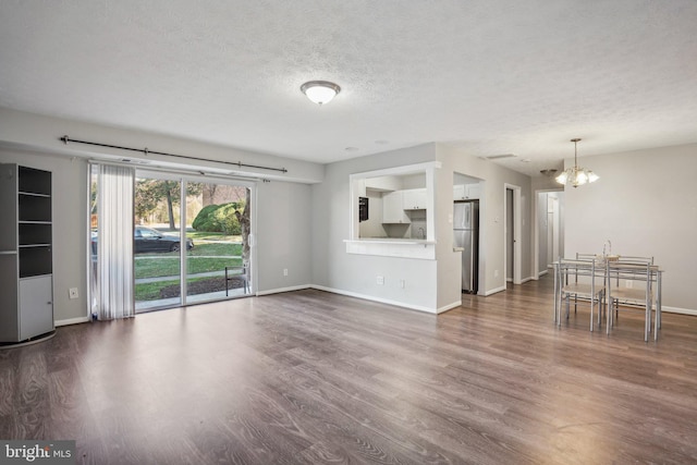 unfurnished living room featuring a textured ceiling, dark hardwood / wood-style flooring, and an inviting chandelier