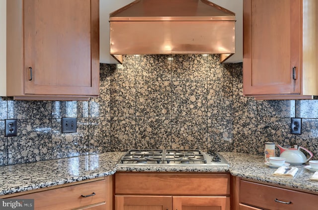 kitchen with island exhaust hood, stainless steel gas stovetop, light stone countertops, and backsplash