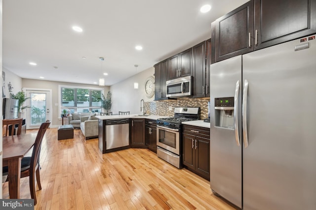 kitchen with kitchen peninsula, decorative backsplash, stainless steel appliances, pendant lighting, and light hardwood / wood-style floors