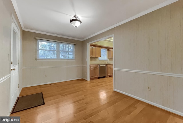 unfurnished dining area featuring wood walls, light wood-type flooring, crown molding, and sink