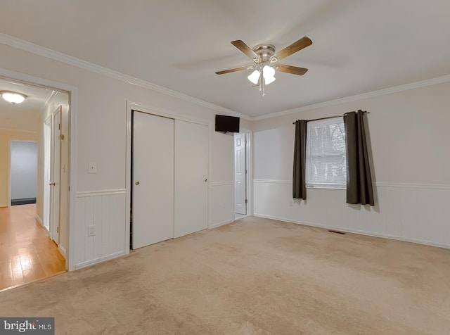 unfurnished bedroom with light carpet, a closet, ceiling fan, and crown molding