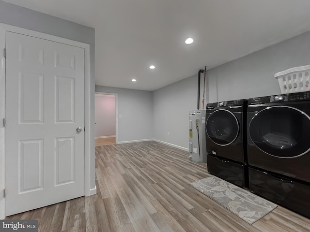 washroom featuring washing machine and dryer, water heater, and light hardwood / wood-style flooring