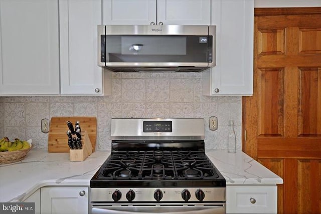 kitchen with white cabinets, backsplash, light stone counters, and stainless steel appliances