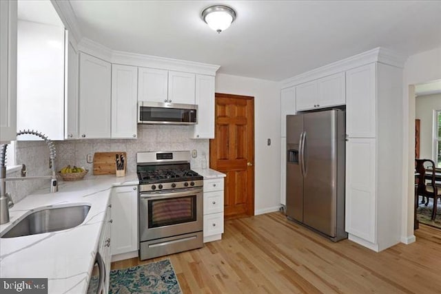 kitchen featuring appliances with stainless steel finishes, tasteful backsplash, sink, light hardwood / wood-style flooring, and white cabinetry