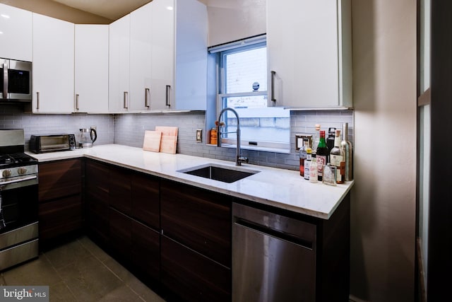 kitchen with light stone countertops, sink, stainless steel appliances, decorative backsplash, and white cabinets