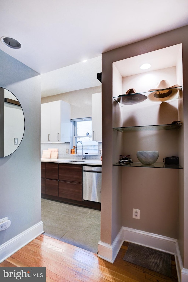 kitchen featuring white cabinetry, sink, stainless steel dishwasher, dark brown cabinets, and light wood-type flooring