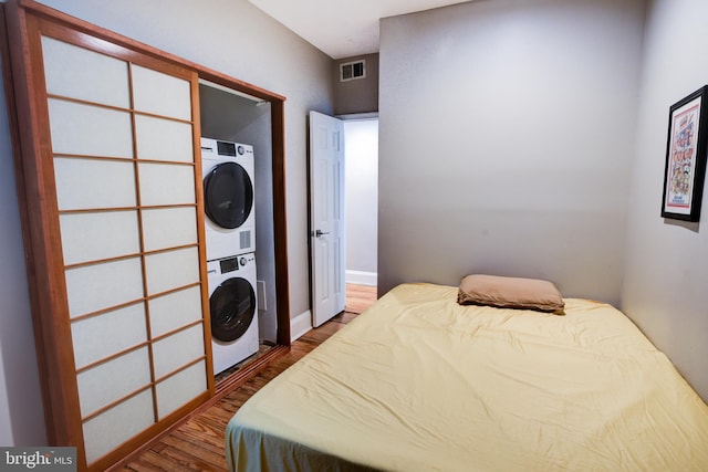 bedroom with wood-type flooring and stacked washer / drying machine