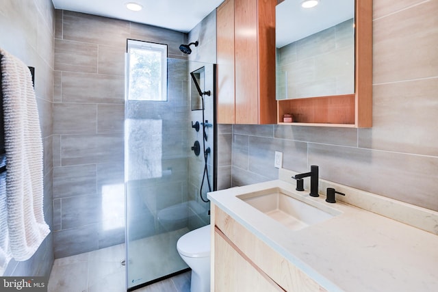 bathroom featuring tasteful backsplash, a tile shower, vanity, tile walls, and toilet