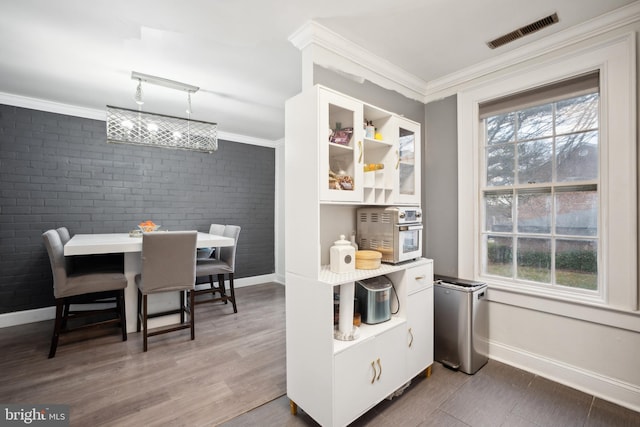 kitchen with white cabinets, ornamental molding, dark wood-type flooring, and brick wall