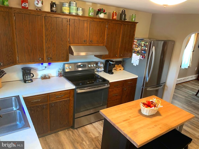 kitchen with sink, baseboard heating, ventilation hood, light hardwood / wood-style floors, and appliances with stainless steel finishes