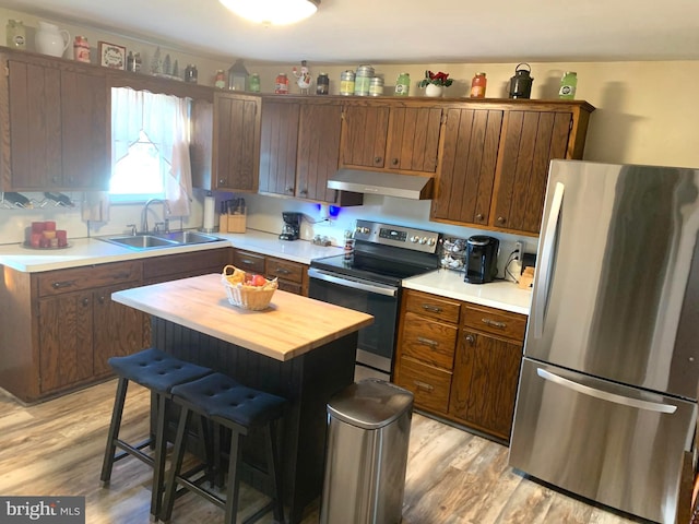 kitchen with sink, a center island, a kitchen breakfast bar, light hardwood / wood-style floors, and appliances with stainless steel finishes