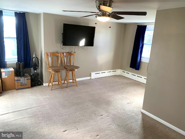 unfurnished living room with carpet, a baseboard heating unit, ceiling fan, and a healthy amount of sunlight