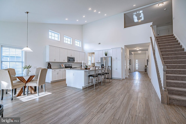 kitchen featuring a center island, high vaulted ceiling, light hardwood / wood-style floors, white cabinetry, and stainless steel appliances