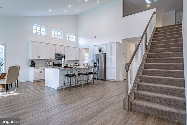 kitchen with high vaulted ceiling, a breakfast bar area, an island with sink, white cabinetry, and stainless steel appliances