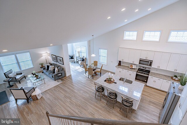 kitchen with light stone countertops, white cabinetry, light hardwood / wood-style floors, a breakfast bar, and appliances with stainless steel finishes