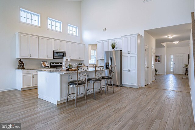 kitchen with light wood-type flooring, stainless steel appliances, white cabinets, a high ceiling, and a center island