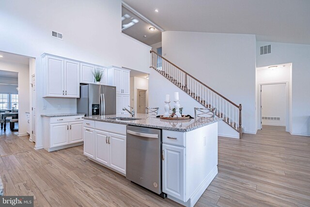 kitchen featuring a kitchen island with sink, white cabinets, sink, light hardwood / wood-style flooring, and appliances with stainless steel finishes