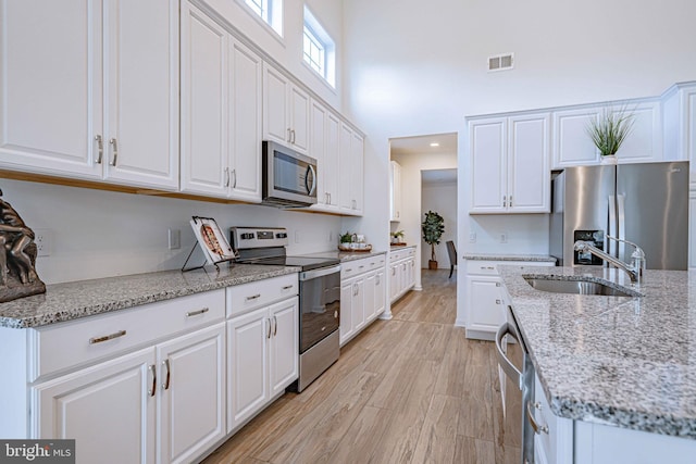 kitchen with sink, light stone countertops, light wood-type flooring, white cabinetry, and stainless steel appliances