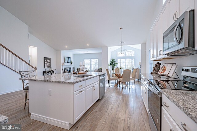 kitchen featuring light wood-type flooring, stainless steel appliances, pendant lighting, white cabinets, and an island with sink