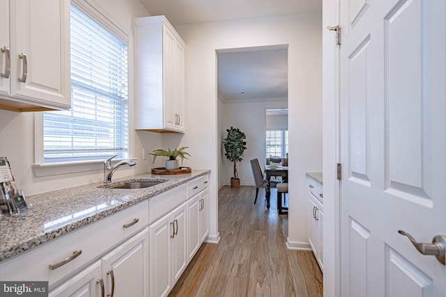 kitchen with light stone counters, sink, white cabinets, and light hardwood / wood-style floors