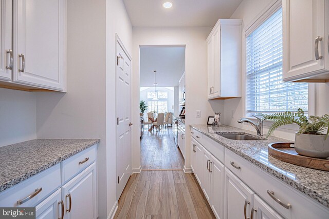 kitchen with light stone countertops, light hardwood / wood-style flooring, white cabinetry, and sink