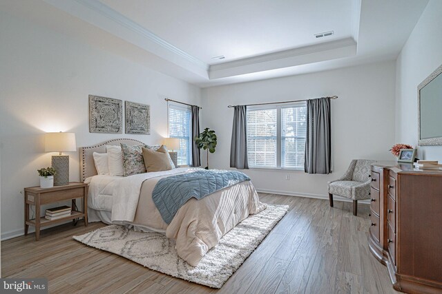 bedroom with a raised ceiling, light wood-type flooring, and ornamental molding