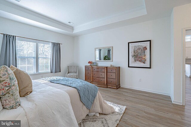 bedroom with light hardwood / wood-style floors, a raised ceiling, and crown molding