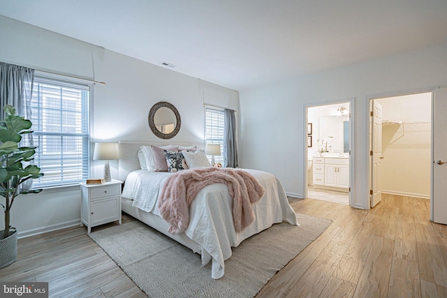 bedroom with a closet, multiple windows, a spacious closet, and light hardwood / wood-style flooring