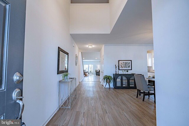 foyer with a towering ceiling, ornamental molding, and light hardwood / wood-style flooring