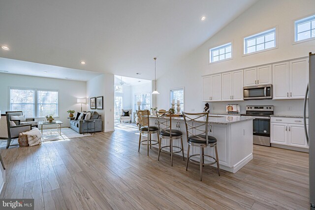 kitchen with appliances with stainless steel finishes, a kitchen breakfast bar, decorative light fixtures, white cabinets, and light hardwood / wood-style floors