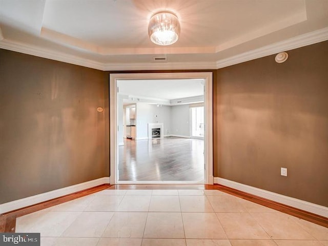 spare room with a tray ceiling, light wood-type flooring, and ornamental molding