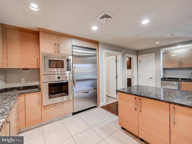 kitchen with light brown cabinets, built in appliances, and dark stone counters