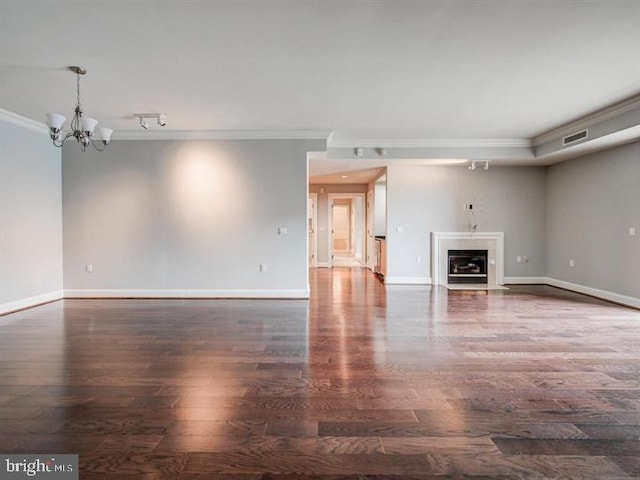 unfurnished living room featuring crown molding, rail lighting, dark hardwood / wood-style floors, and an inviting chandelier