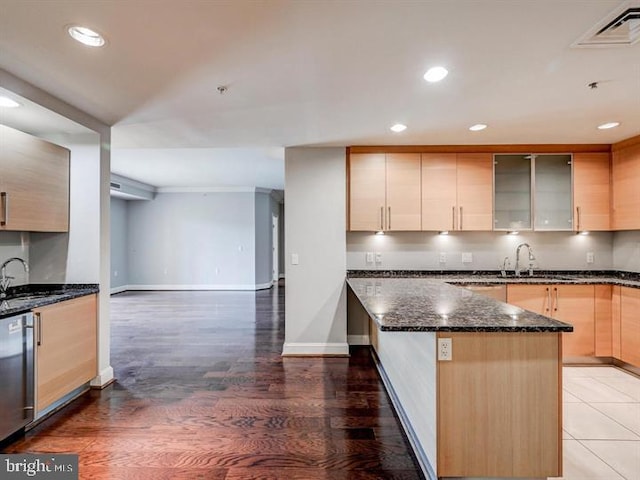 kitchen with light brown cabinets, dark stone counters, sink, stainless steel dishwasher, and dark hardwood / wood-style floors