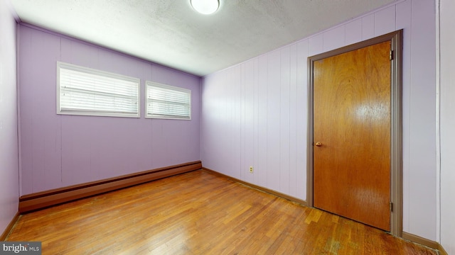 unfurnished bedroom with wood walls, light hardwood / wood-style floors, a textured ceiling, and a baseboard heating unit