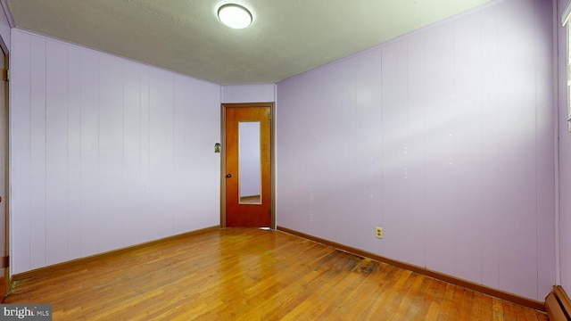 unfurnished room featuring hardwood / wood-style flooring, wooden walls, and a baseboard heating unit