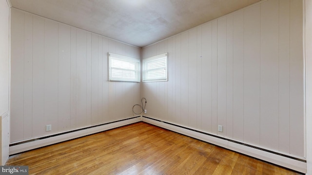 unfurnished room featuring light wood-type flooring, a baseboard radiator, and wood walls