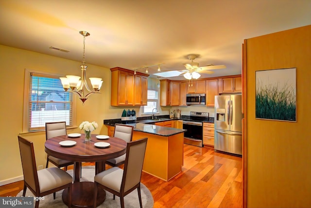 kitchen with kitchen peninsula, light hardwood / wood-style flooring, decorative light fixtures, sink, and appliances with stainless steel finishes