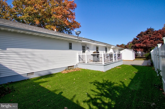 rear view of house featuring a yard, a wooden deck, and a storage shed