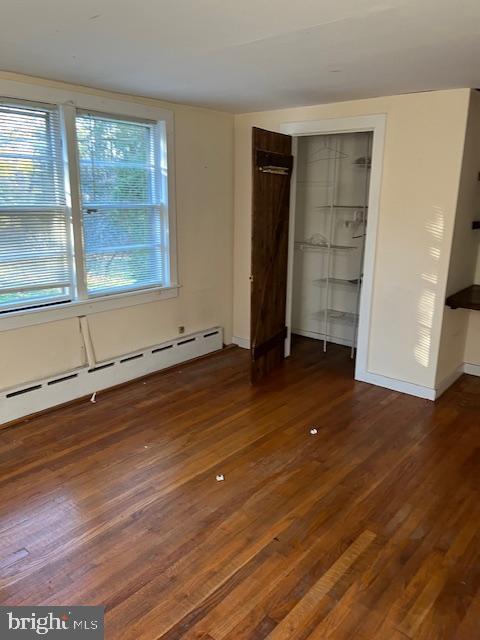 unfurnished bedroom featuring a baseboard radiator, a closet, and dark wood-type flooring