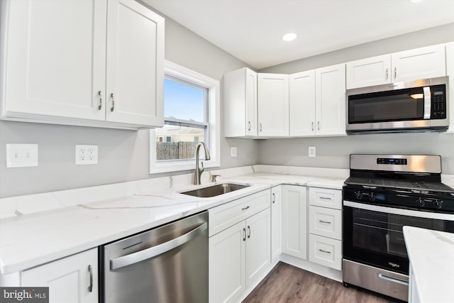 kitchen with sink, dark hardwood / wood-style floors, appliances with stainless steel finishes, light stone counters, and white cabinetry