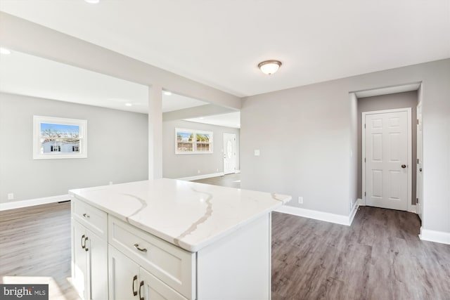 kitchen featuring white cabinets, a center island, light stone counters, and light hardwood / wood-style flooring