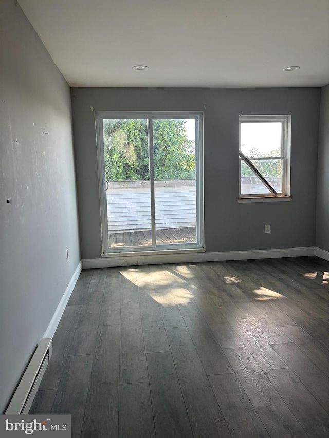 empty room featuring dark hardwood / wood-style flooring, a baseboard radiator, and plenty of natural light