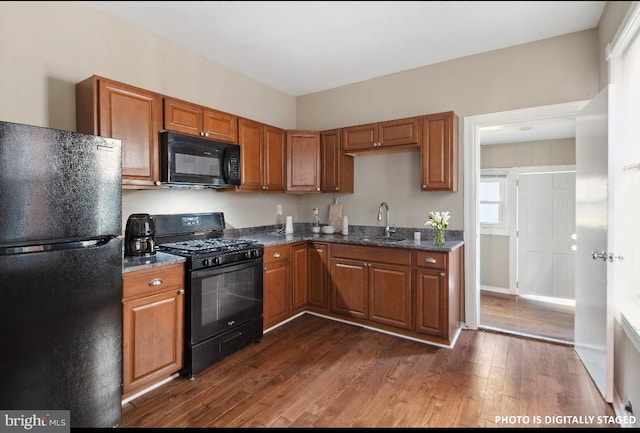 kitchen featuring black appliances, sink, dark wood-type flooring, and dark stone counters