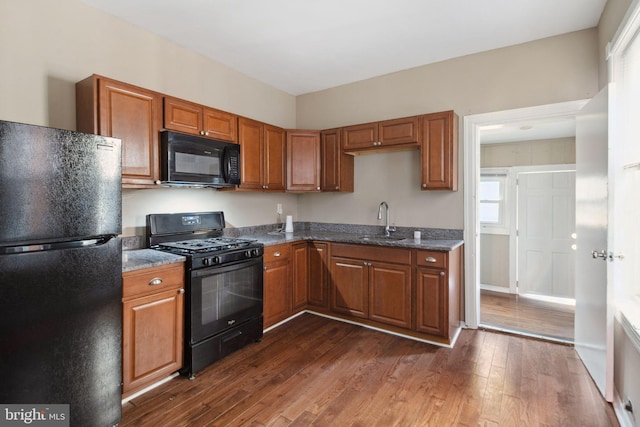 kitchen featuring dark stone countertops, sink, dark wood-type flooring, and black appliances