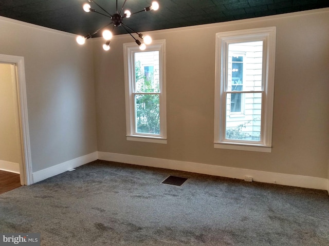 carpeted empty room featuring crown molding, a healthy amount of sunlight, and an inviting chandelier