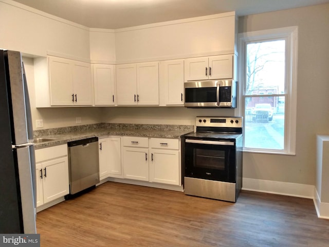 kitchen with white cabinets, crown molding, stainless steel appliances, and light hardwood / wood-style flooring