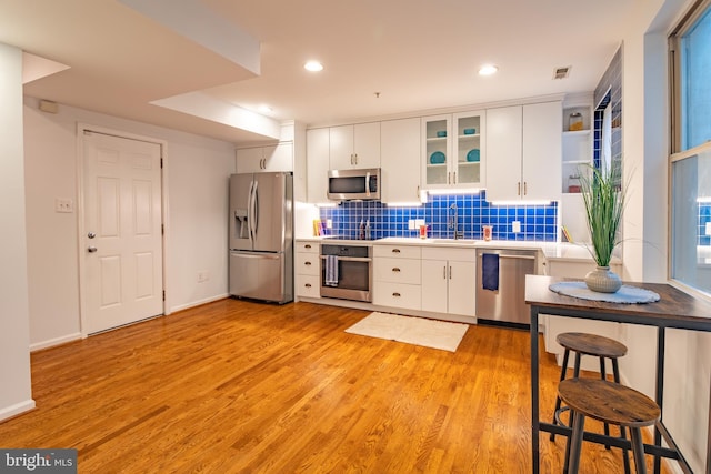 kitchen with white cabinets, sink, light wood-type flooring, appliances with stainless steel finishes, and tasteful backsplash