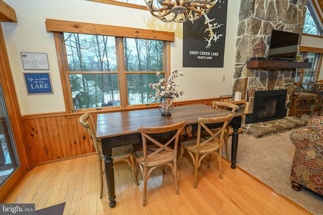 dining space with an inviting chandelier, light hardwood / wood-style floors, a stone fireplace, and a healthy amount of sunlight